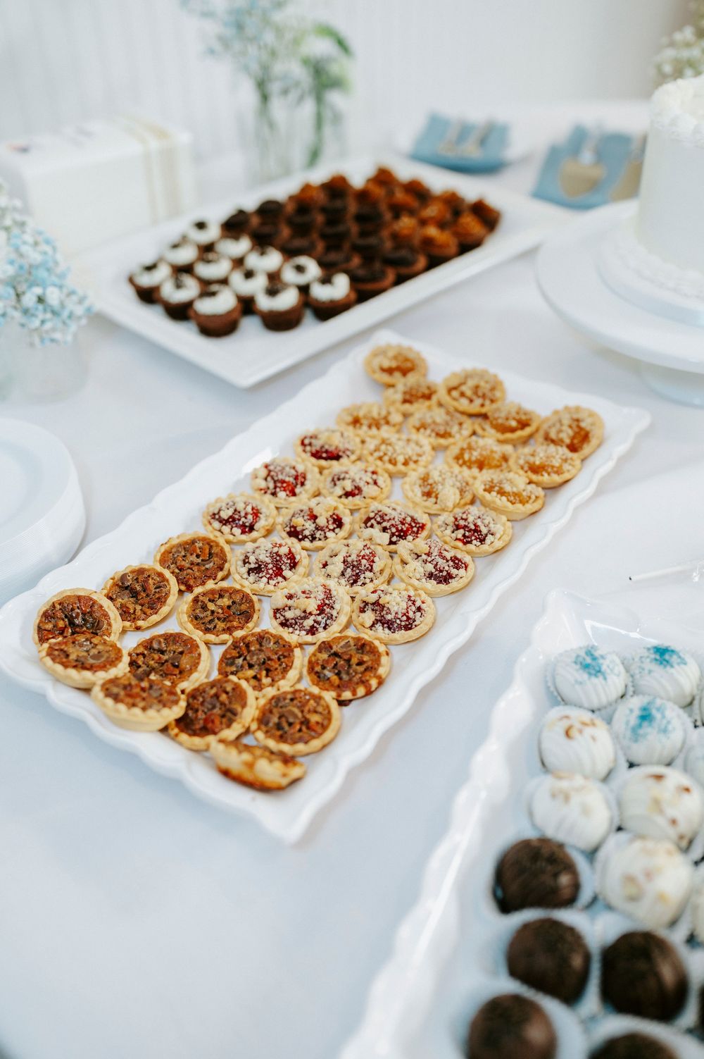 Elegant dessert table with mini tarts, chocolate cupcakes, and cake pops on white platters at a formal event.