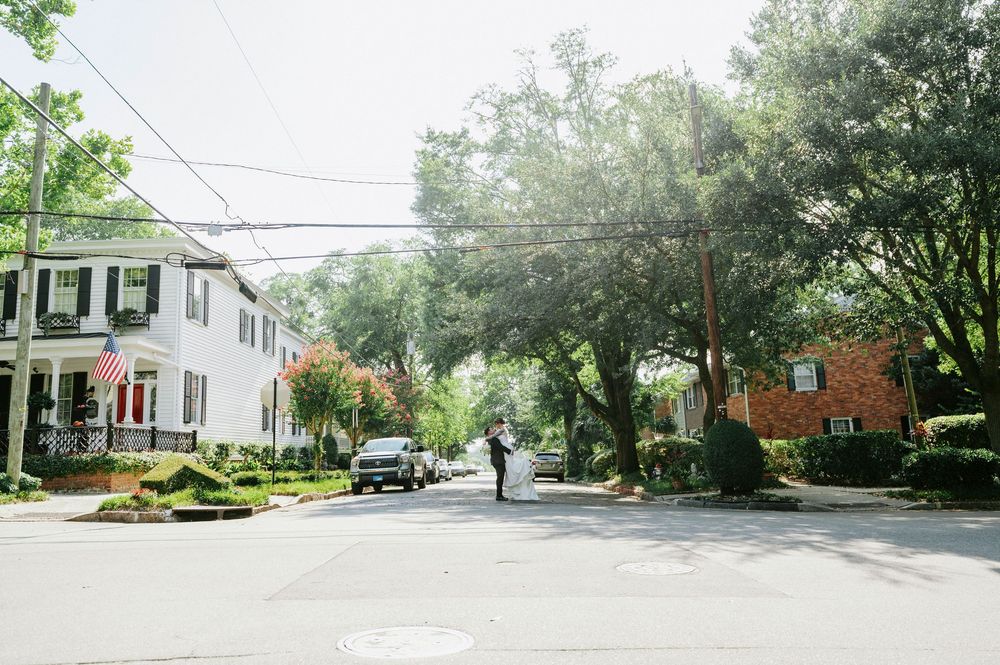 Couple sharing a romantic moment on a tree-lined residential street with historic homes and an American flag on a sunny day.