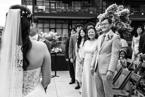 Black and white wedding photo of bride facing groom and smiling family members at outdoor ceremony.