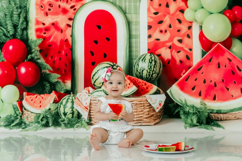 Baby girl sits in a basket at a watermelon-themed birthday photo shoot with colorful decorations.