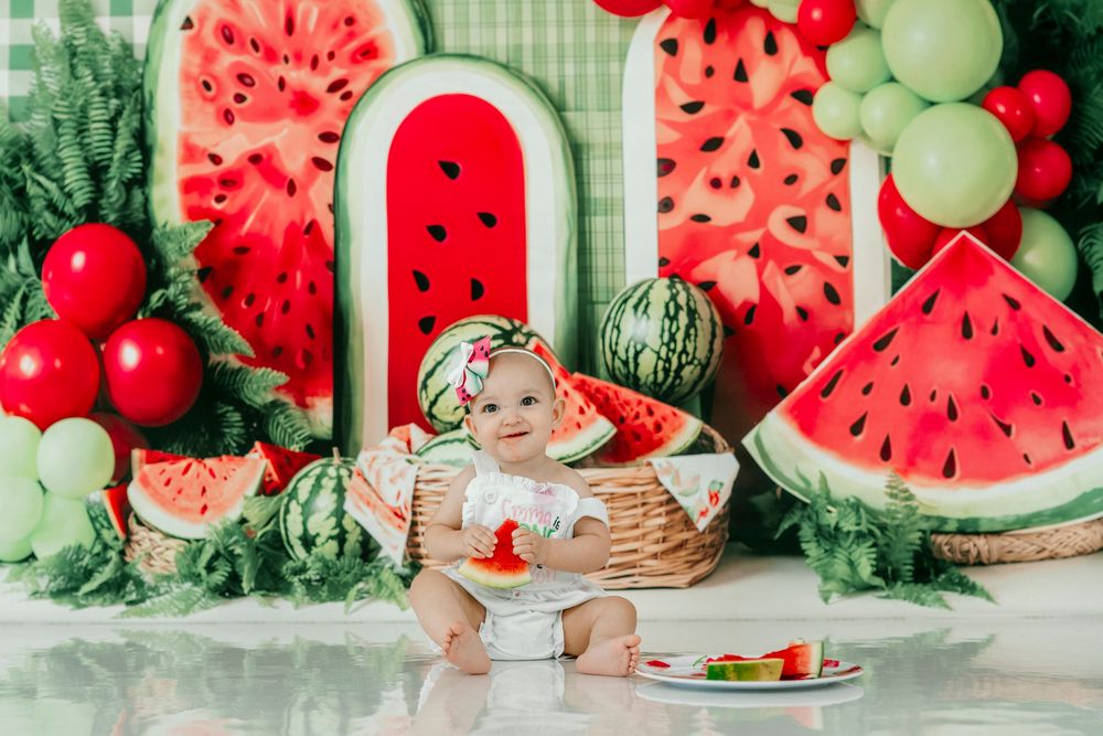Baby girl sitting in basket surrounded by watermelon decorations and balloons at a colorful first birthday cake smash party.
