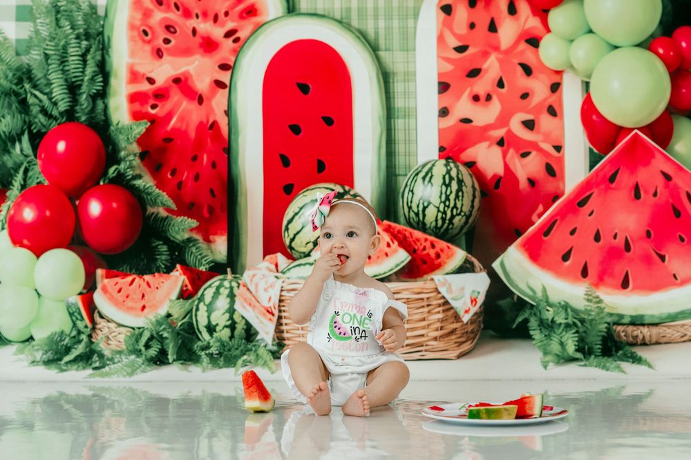 Baby girl in watermelon outfit sits in basket surrounded by colorful watermelon-themed birthday party decorations and balloons.