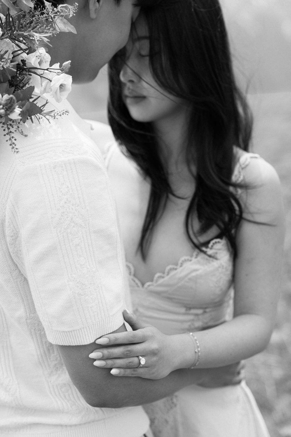 Black and white photo of a couple in white attire sharing an intimate moment, woman wearing an engagement ring.