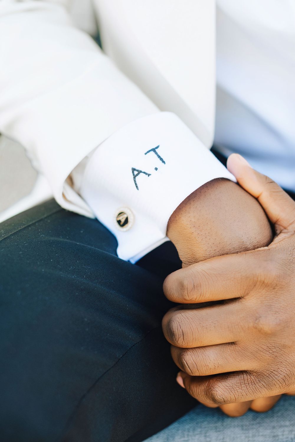 Close-up of monogrammed A.T. cufflink on white dress shirt sleeve with clasped hands.