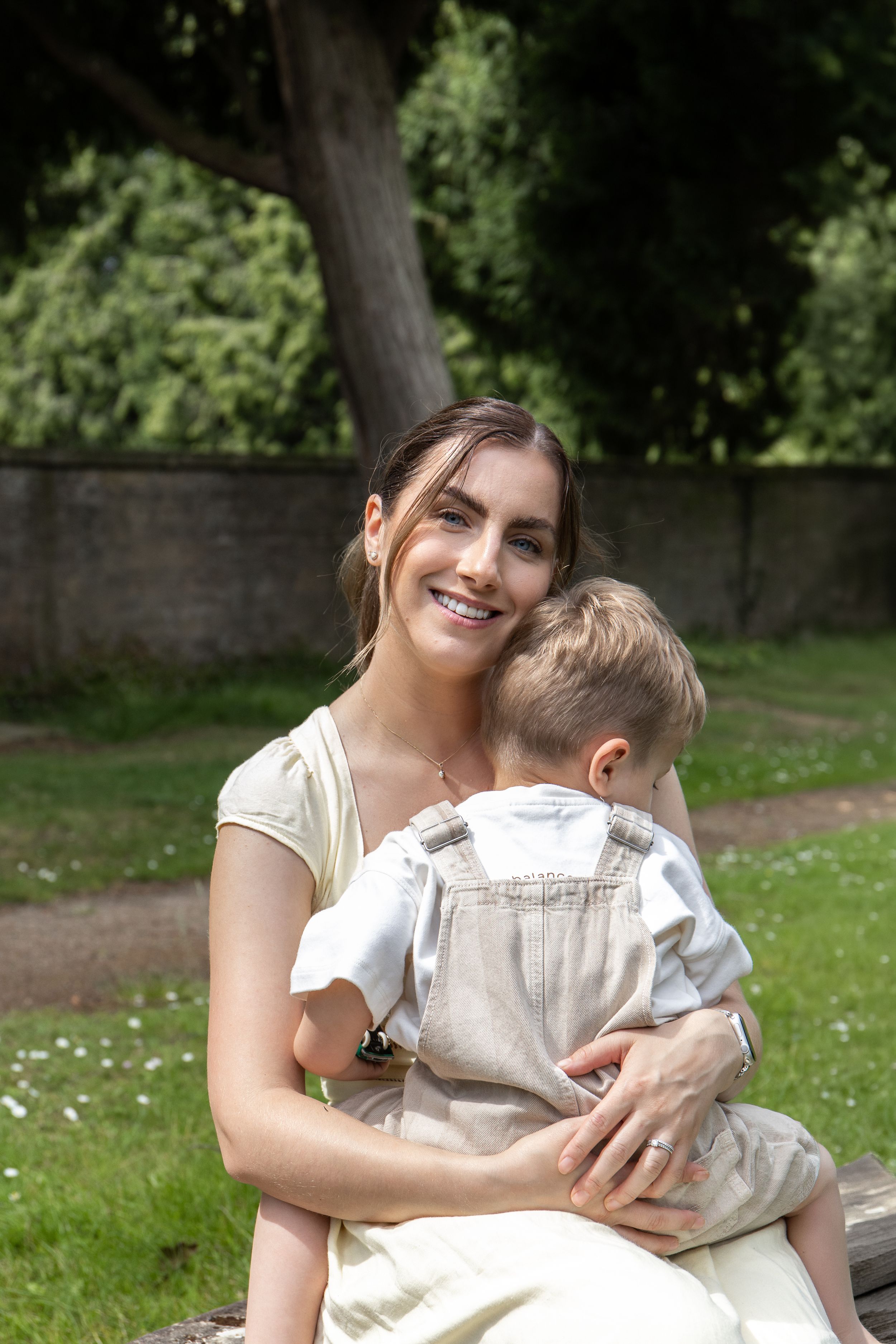 Smiling mother sitting outdoors, lovingly holding her toddler on her lap Outdoor natural family photoshoot Nottingham