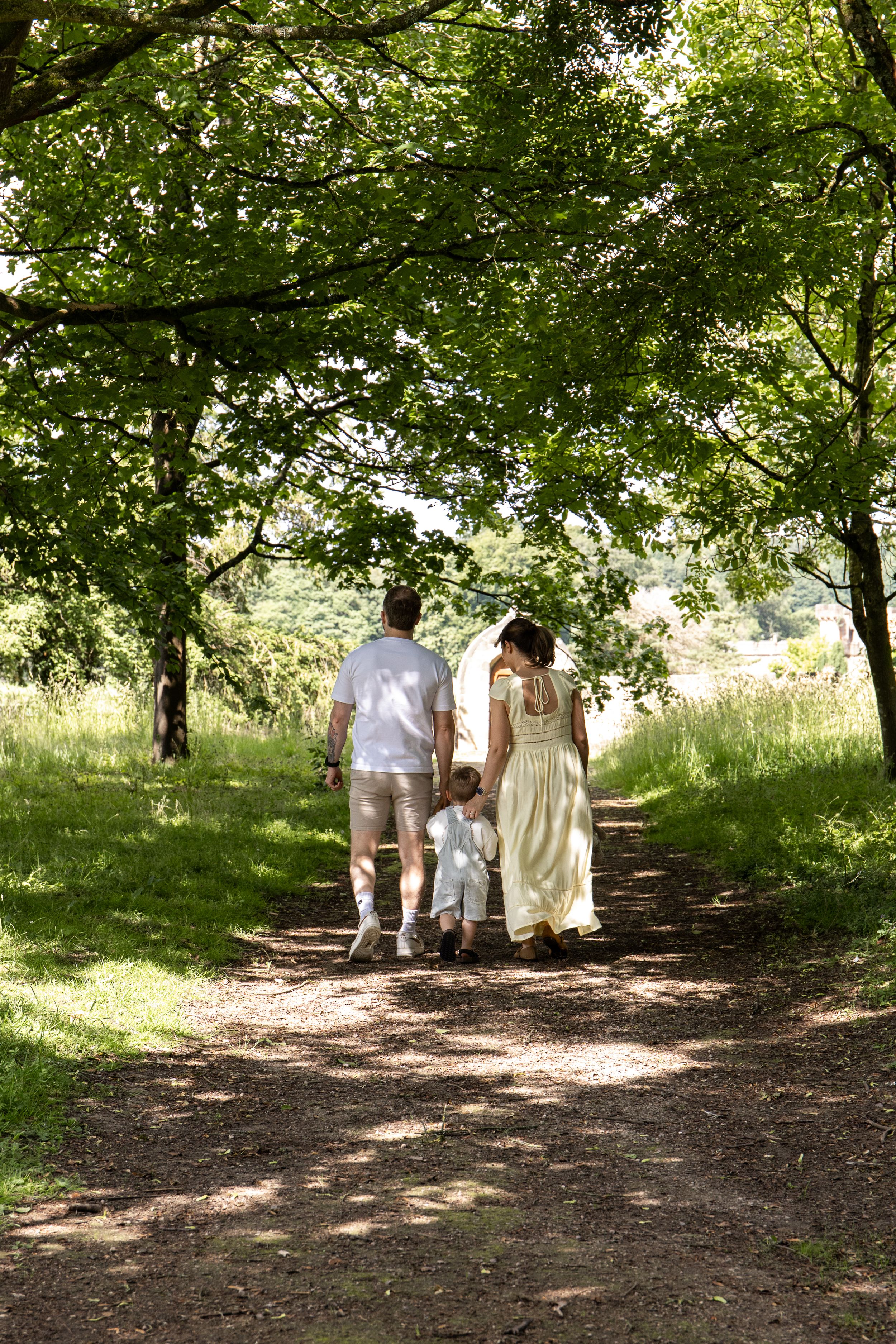 Family walking along a shaded woodland path, parents holding child's hands Outdoor natural family photoshoot Nottingham