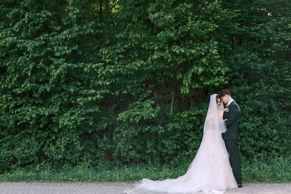 Bride and groom share romantic moment before lush green forest backdrop on wedding day.