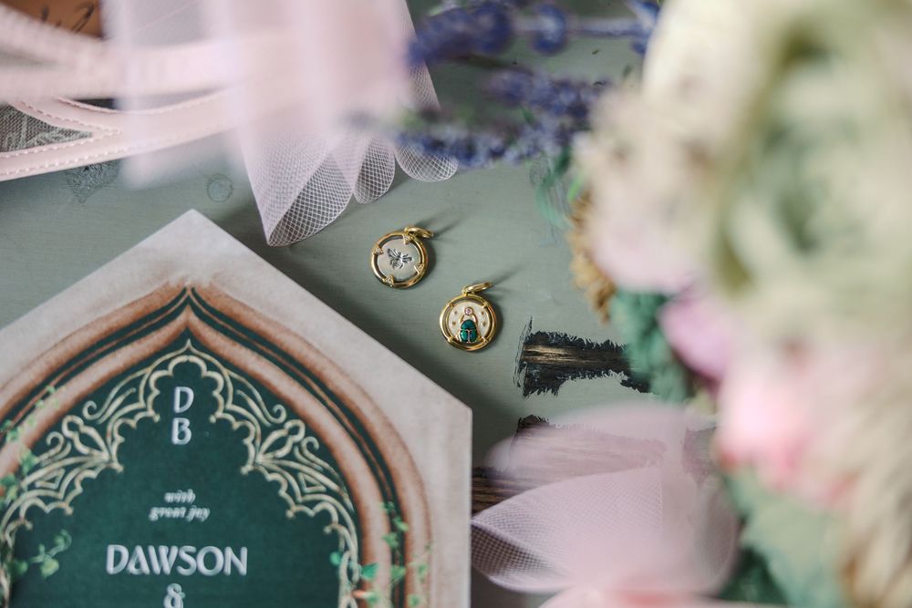 Gold wedding earrings and invitation suite with green botanical design on a styled flat lay.