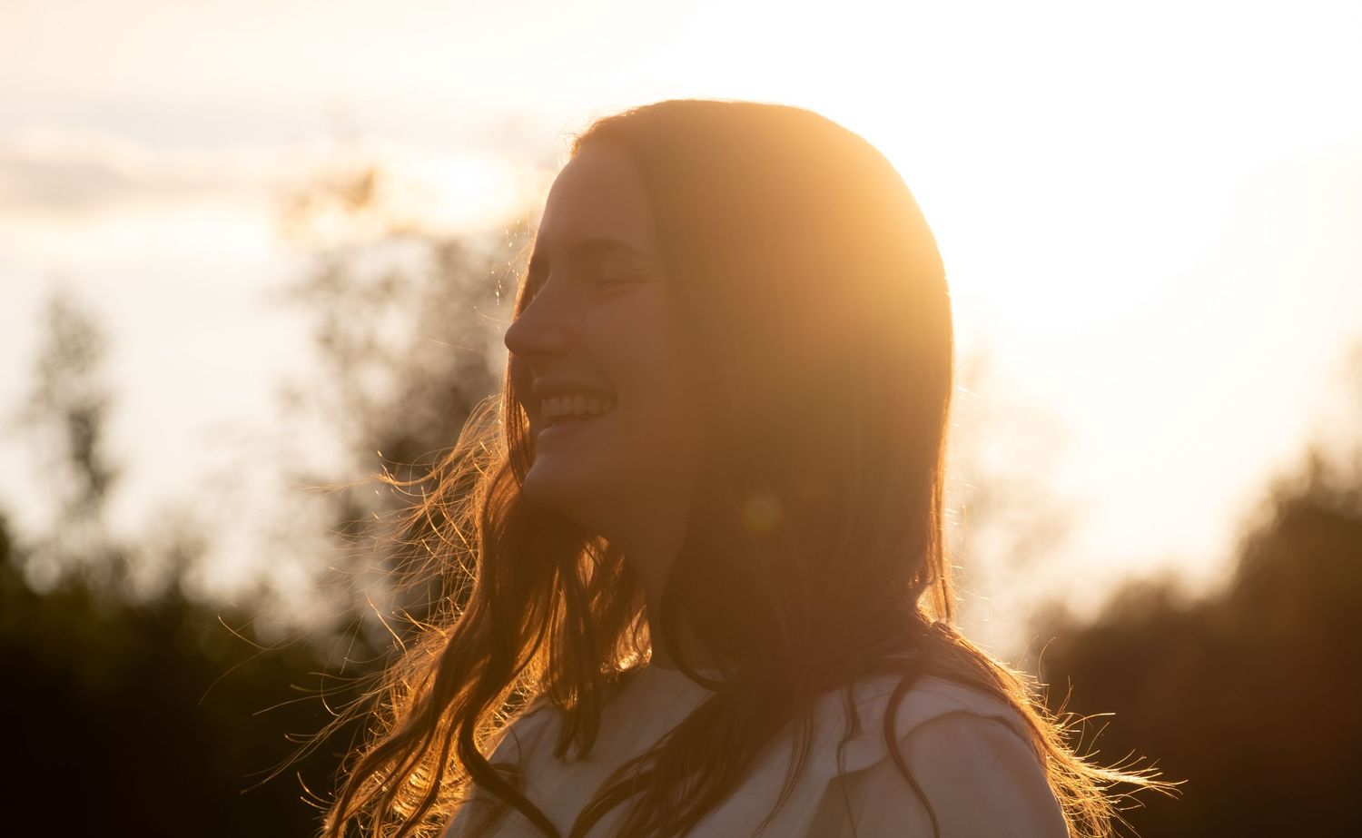 Silhouette of a woman with long hair against a warm golden backlit glow, creating a serene and ethereal portrait.