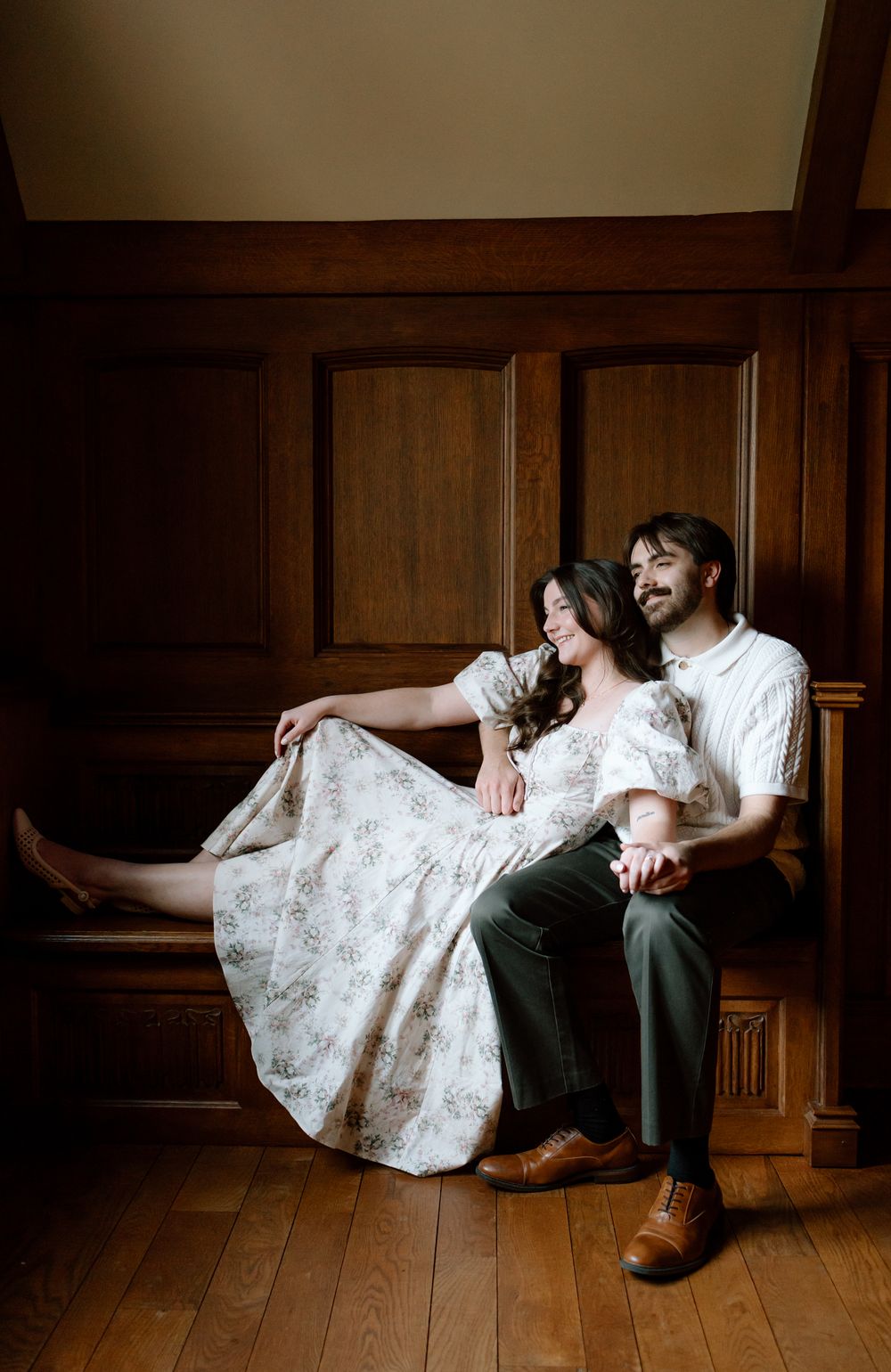 A couple sits together on a wooden bench in an elegant paneled room, smiling warmly.