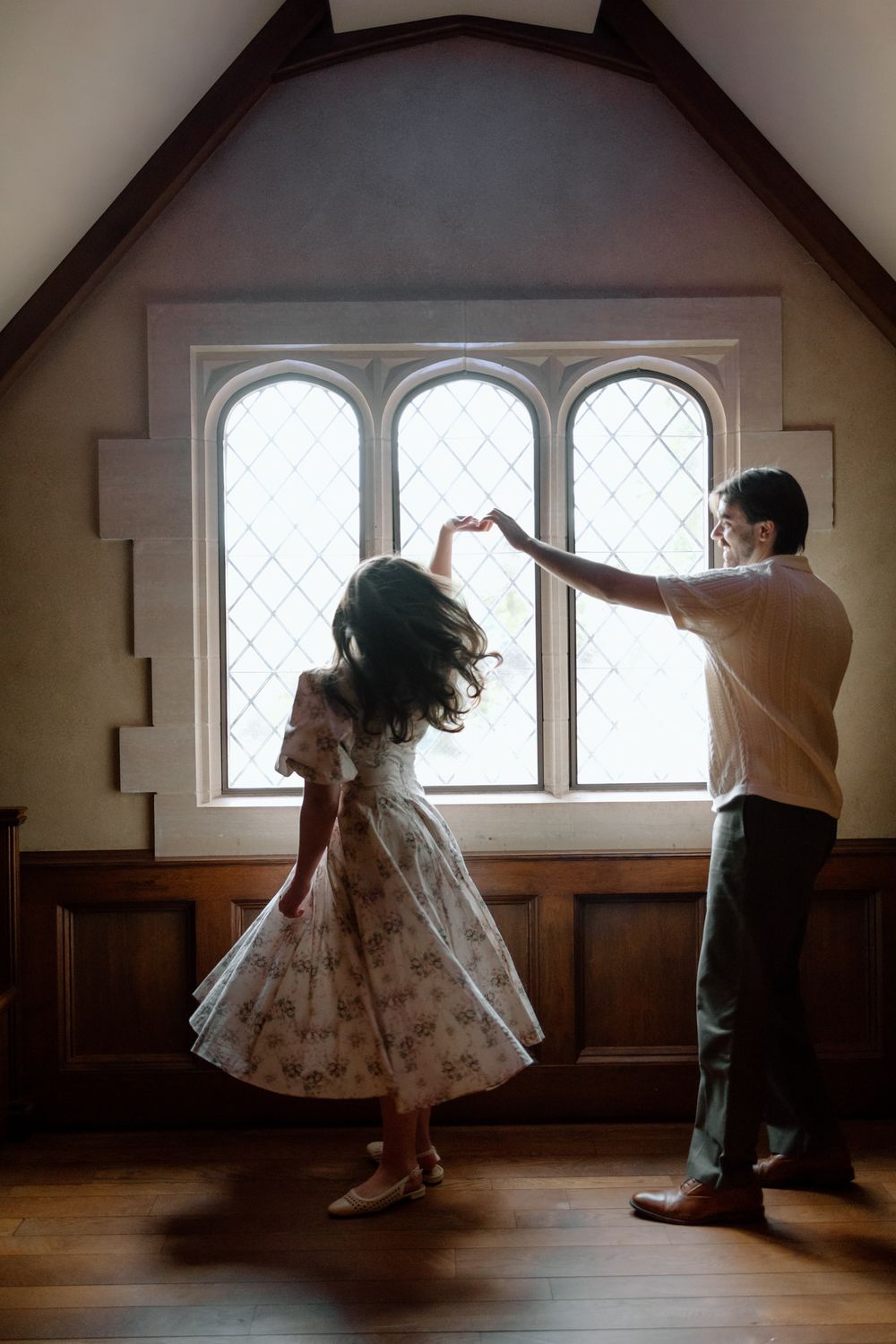 Couple dancing together near a vintage arched window in a warmly lit historic room.