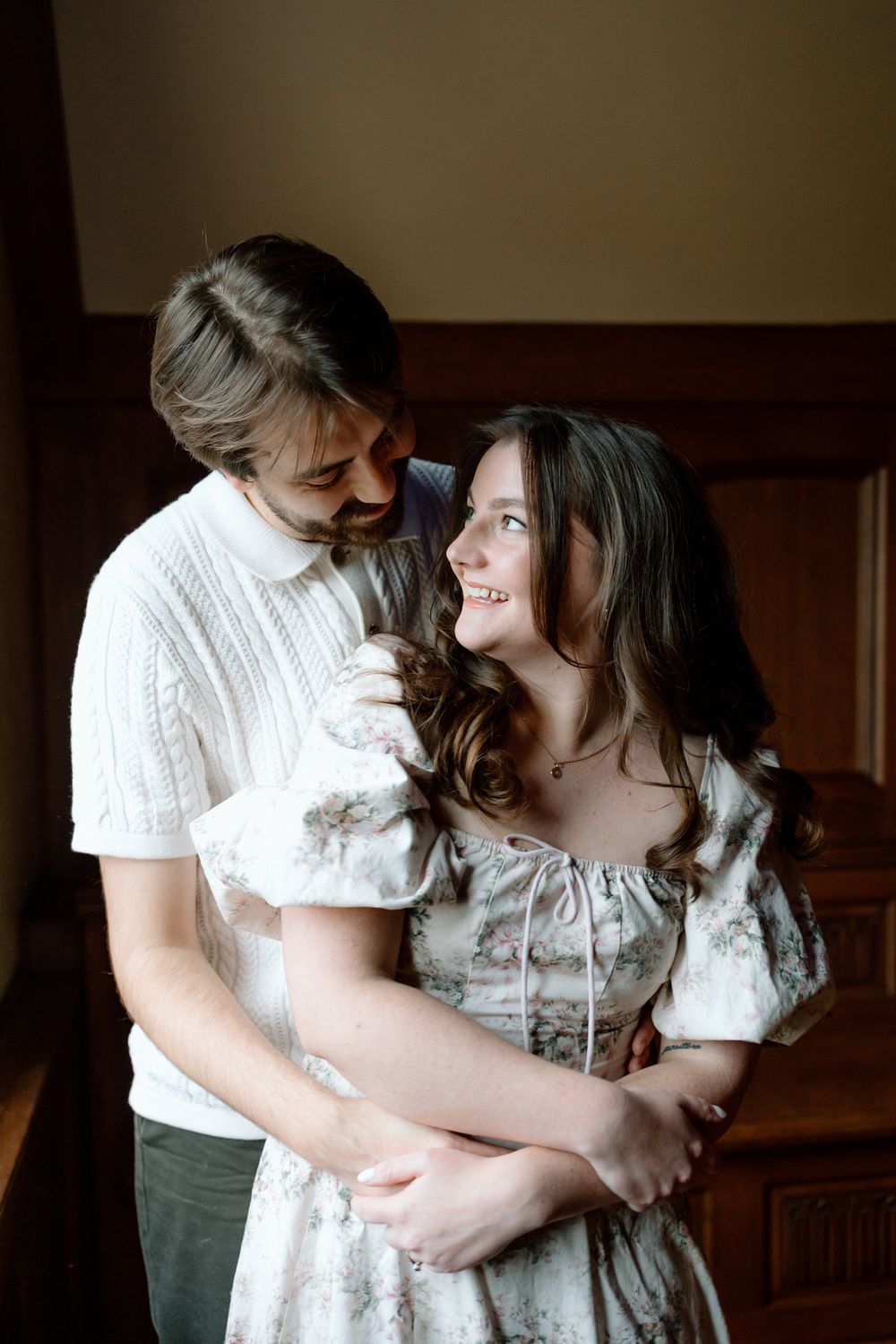 Couple sharing a tender embrace indoors, smiling at each other in soft warm lighting.