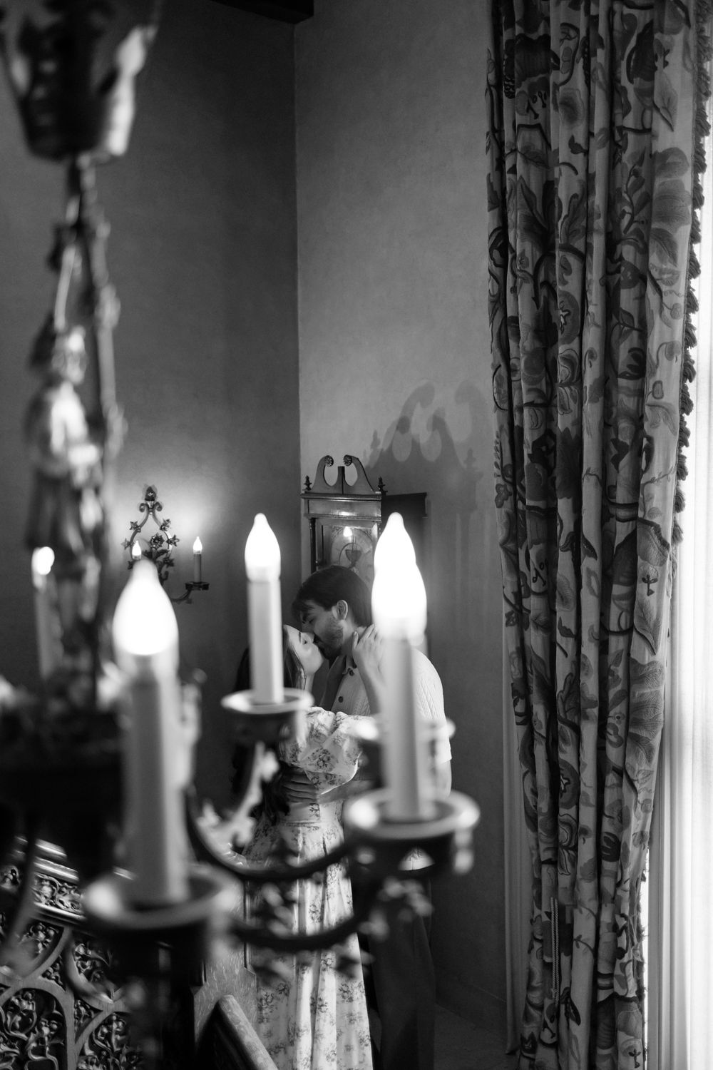 Black and white photo of a woman reflected near a candelabra with glowing candles indoors.