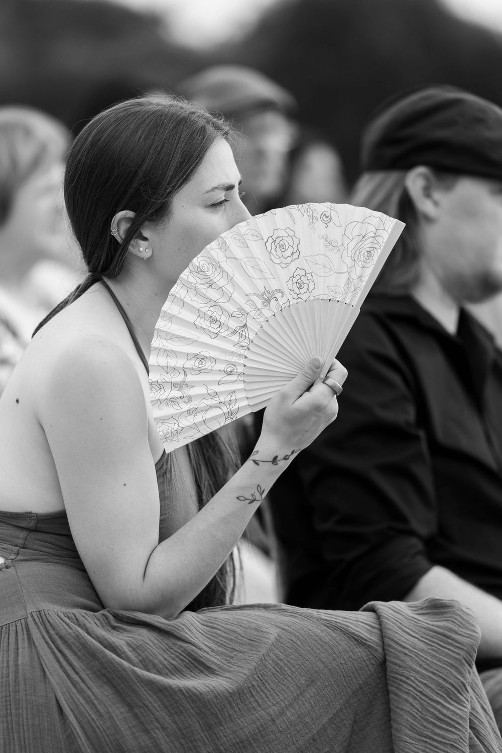 Woman holding decorative lace fan at outdoor wedding ceremony in black and white photo.