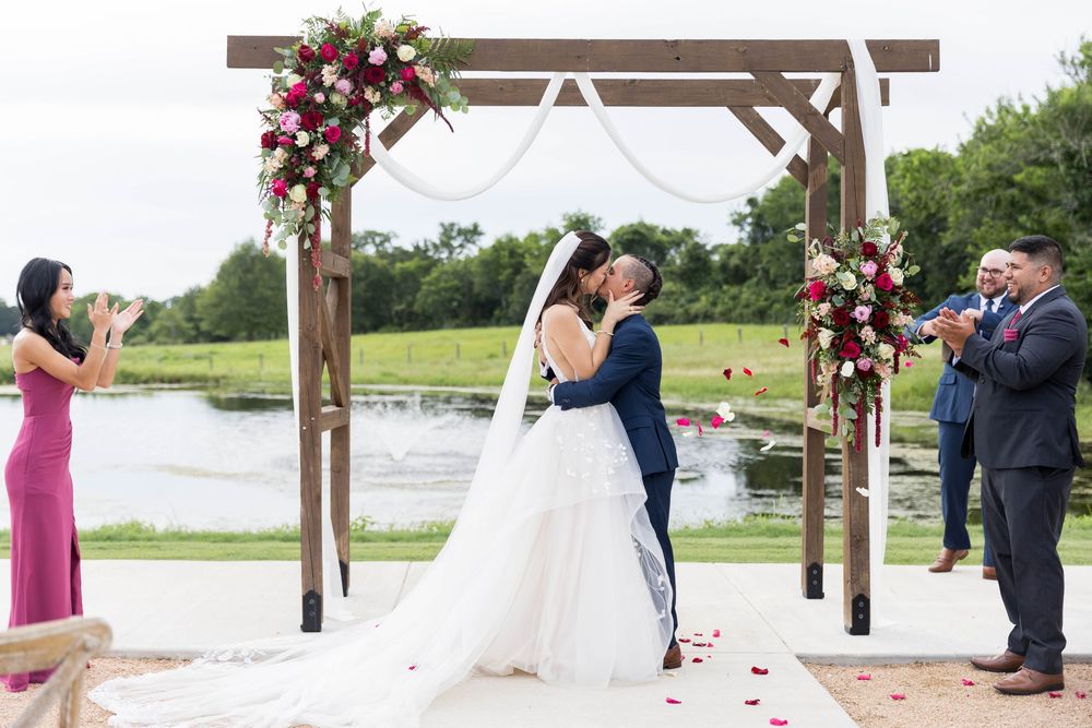 Bride and groom share first kiss under floral arch at outdoor waterfront wedding.