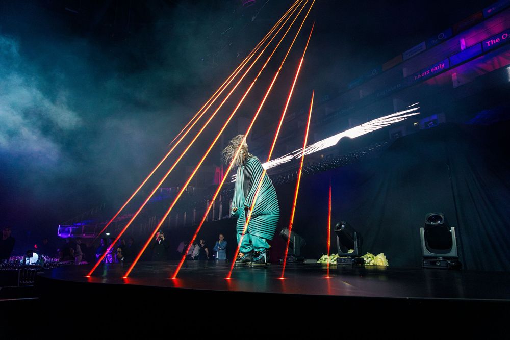 Performer on stage surrounded by dramatic red laser lights during a live concert event.