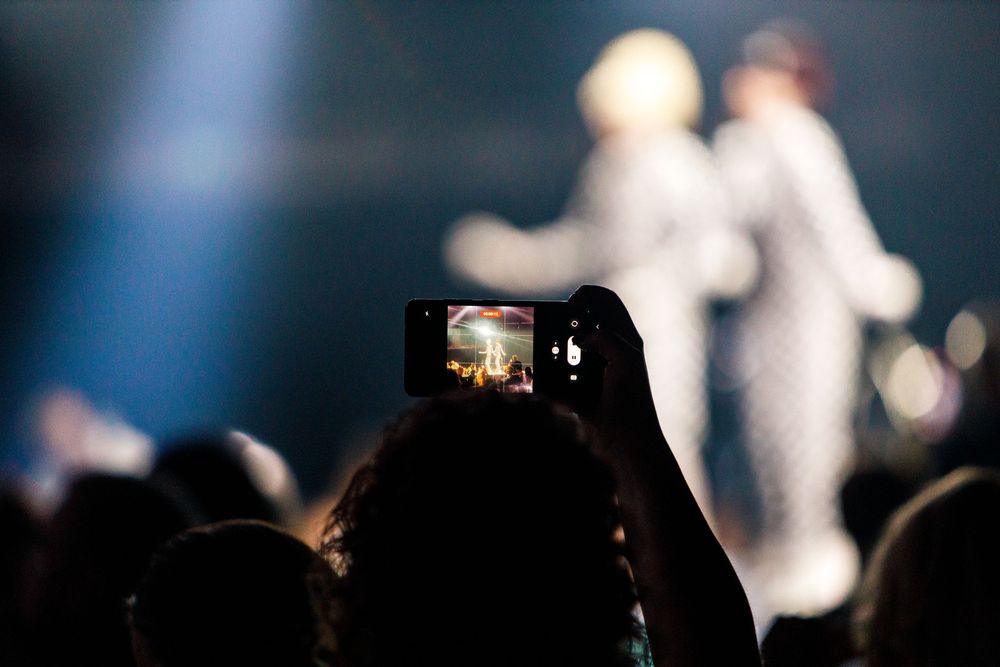 Concert audience member records live performance on smartphone with blurred stage lights.