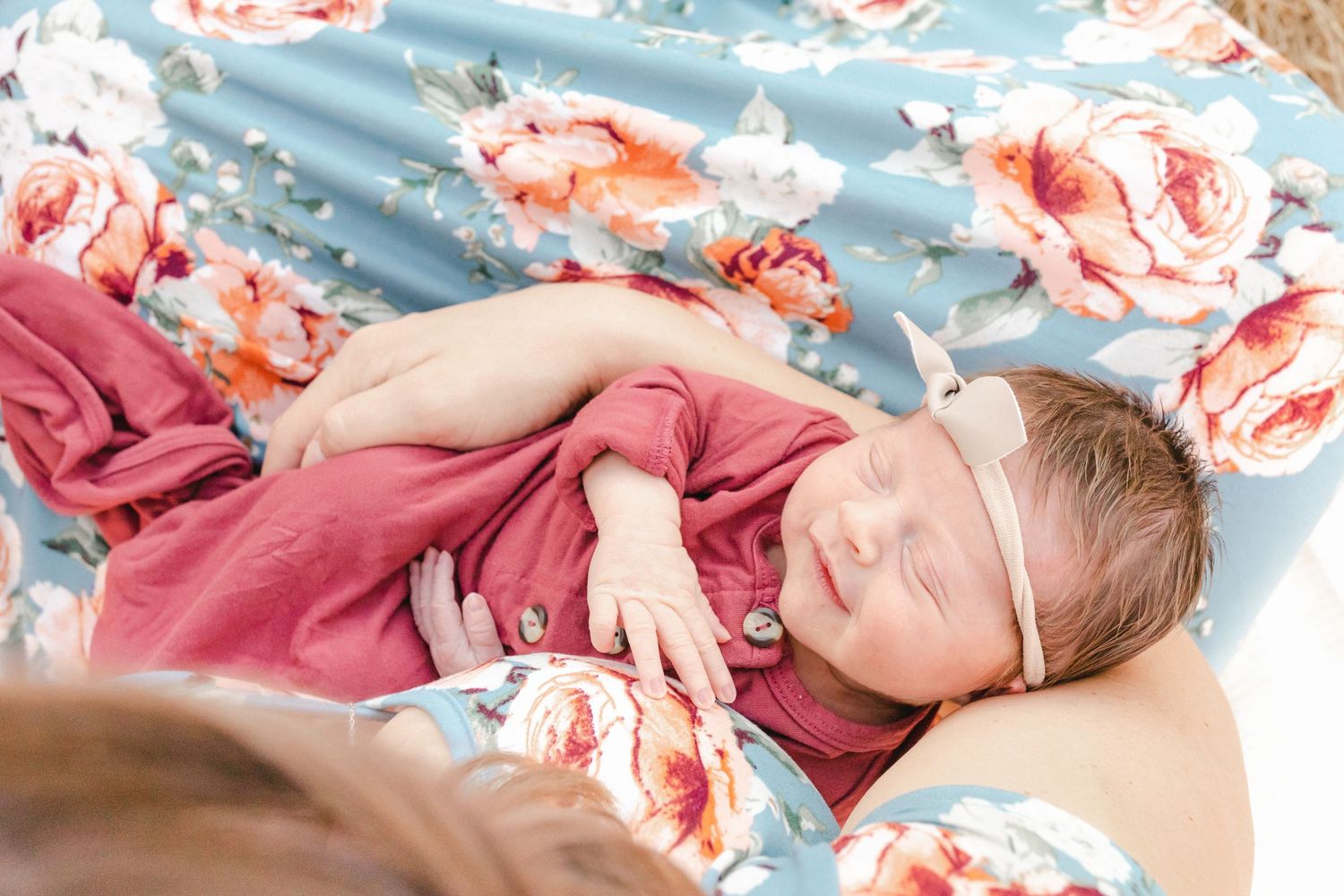 Newborn baby in pink outfit sleeping on floral blue blanket during professional newborn photography session.