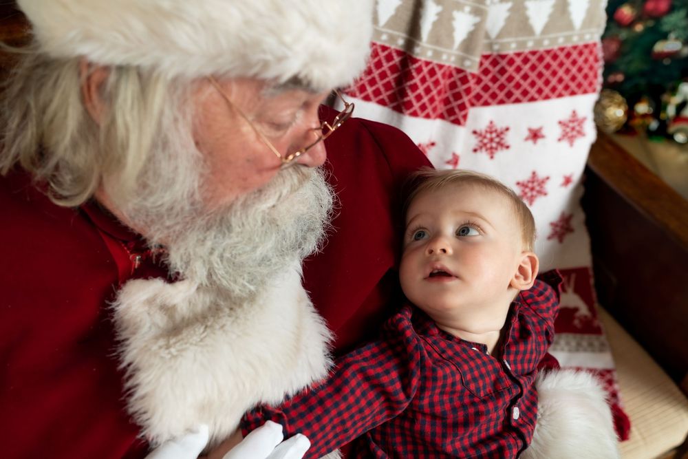 A baby in plaid looks up at Santa Claus during a festive Christmas photo session.
