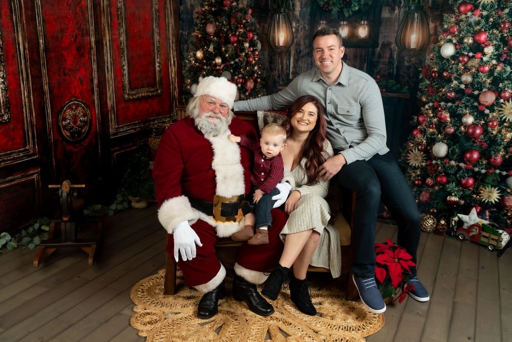 Family posing with Santa Claus in festive Christmas photo studio with decorated trees and holiday decor.