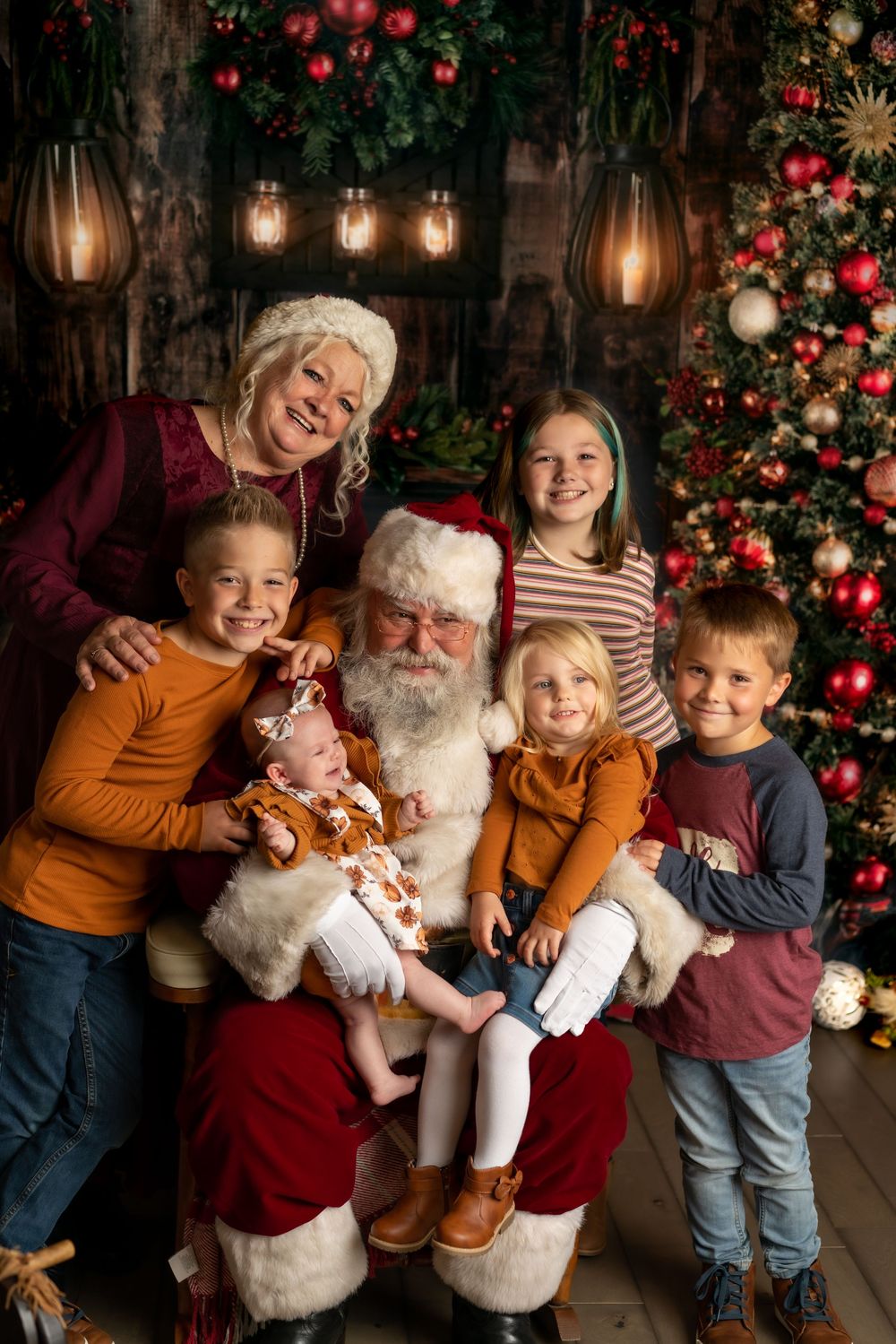 Family posing with Santa and Mrs. Claus by a decorated Christmas tree, featuring five children in festive holiday attire.