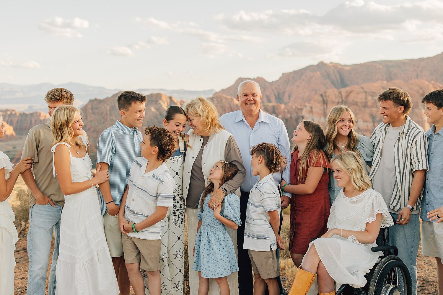 Large extended family group photo at scenic overlook with red rock canyon backdrop at sunset.