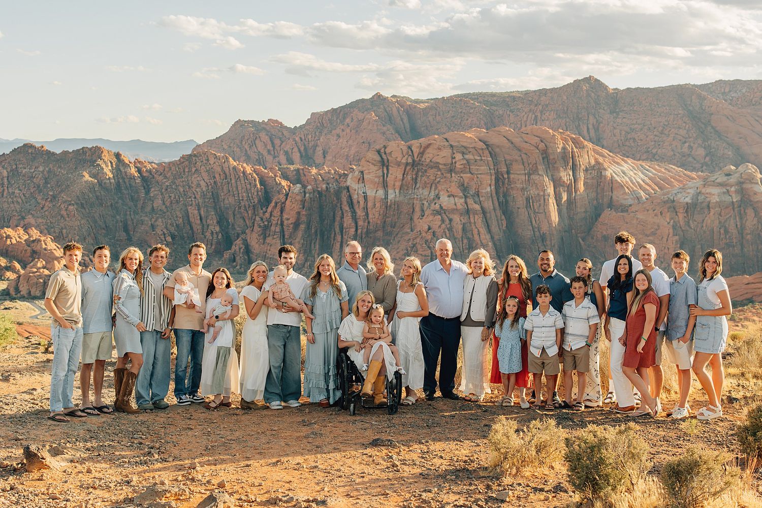 Large family group portrait posed against stunning red rock canyon landscape in warm golden hour light.