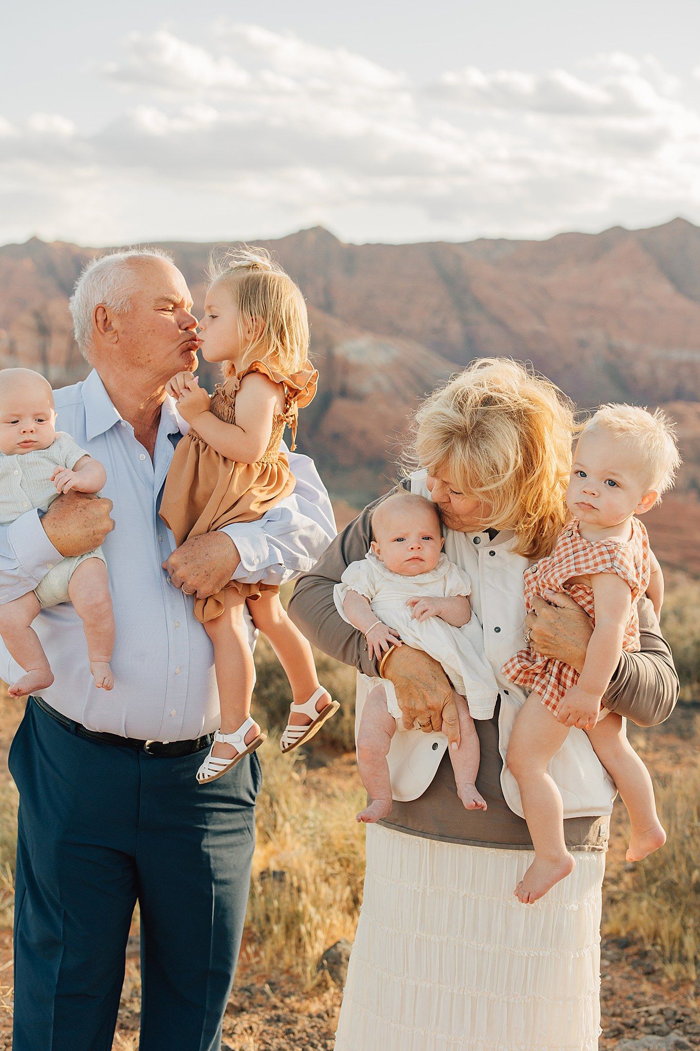 Grandparents holding four young grandchildren outdoors with red rock mountains in the background.