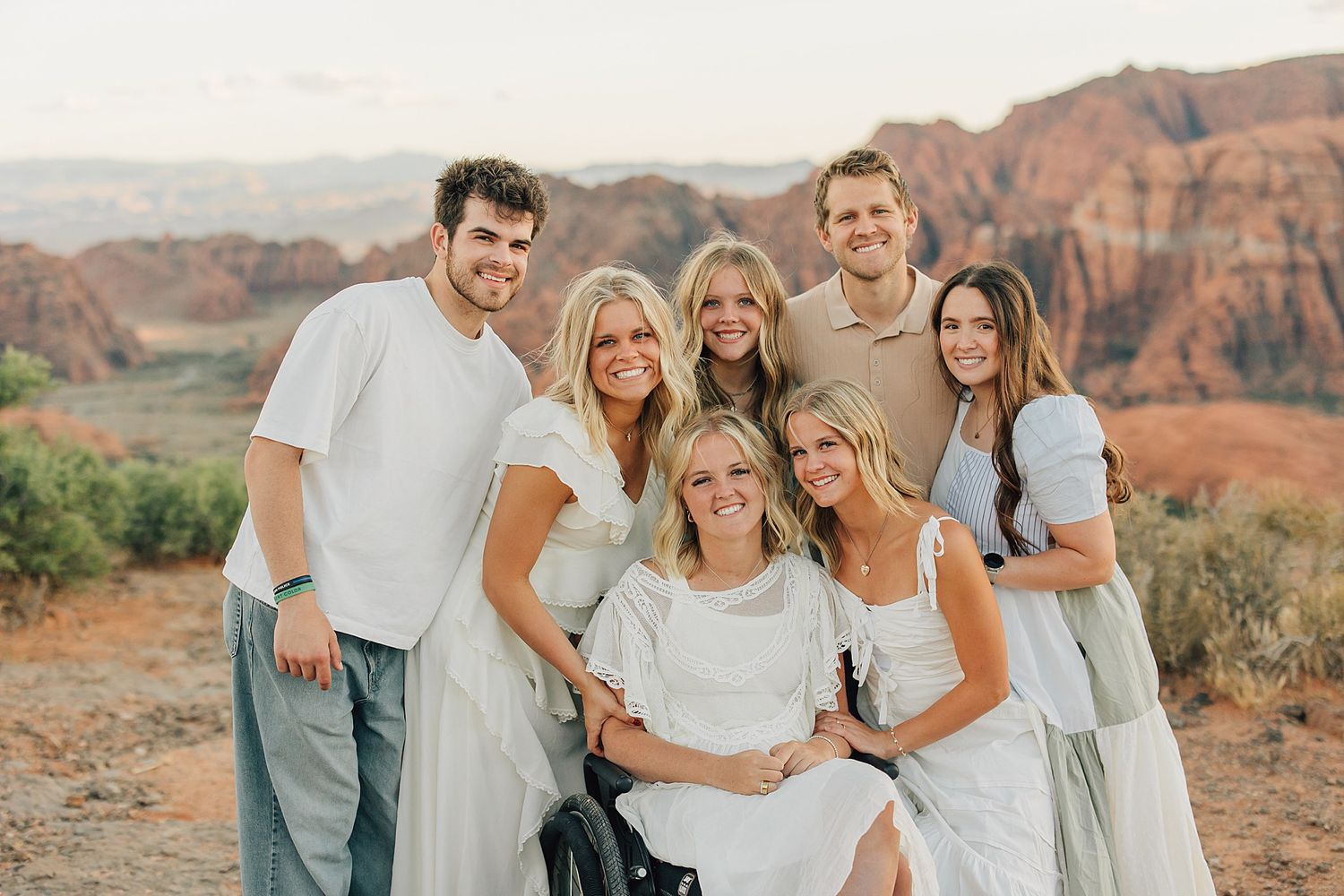 Group of seven smiling people posing together outdoors with red rock canyon landscape in the background.