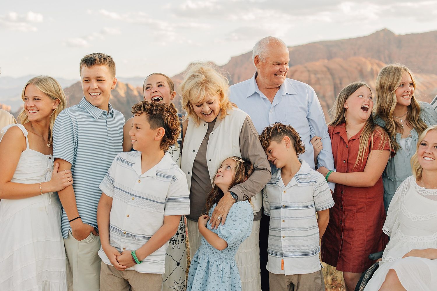 Large multigenerational family smiling together outdoors with scenic red rock canyon landscape in the background.