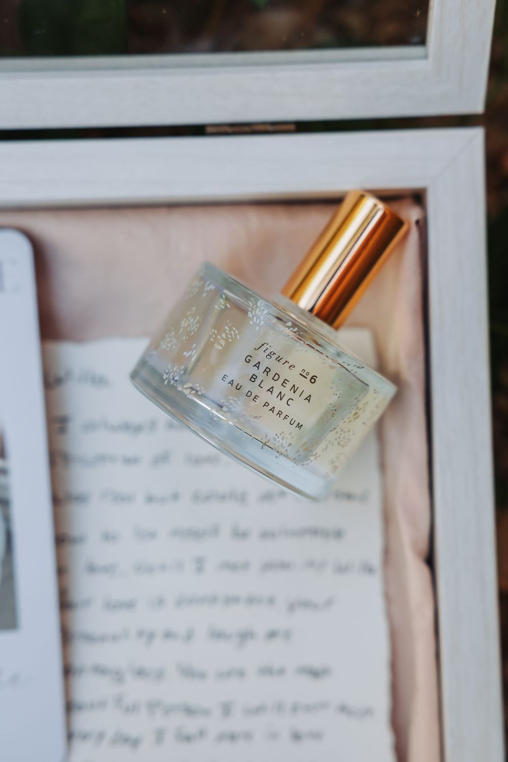 Fleure 46 Gardenia Blanc Eau de Parfum bottle with gold cap resting on a handwritten love letter.