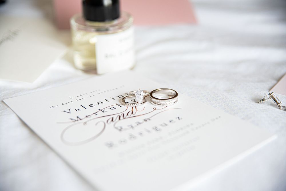 Wedding invitation with gold rings and perfume bottle on white fabric for elegant bridal flat lay.