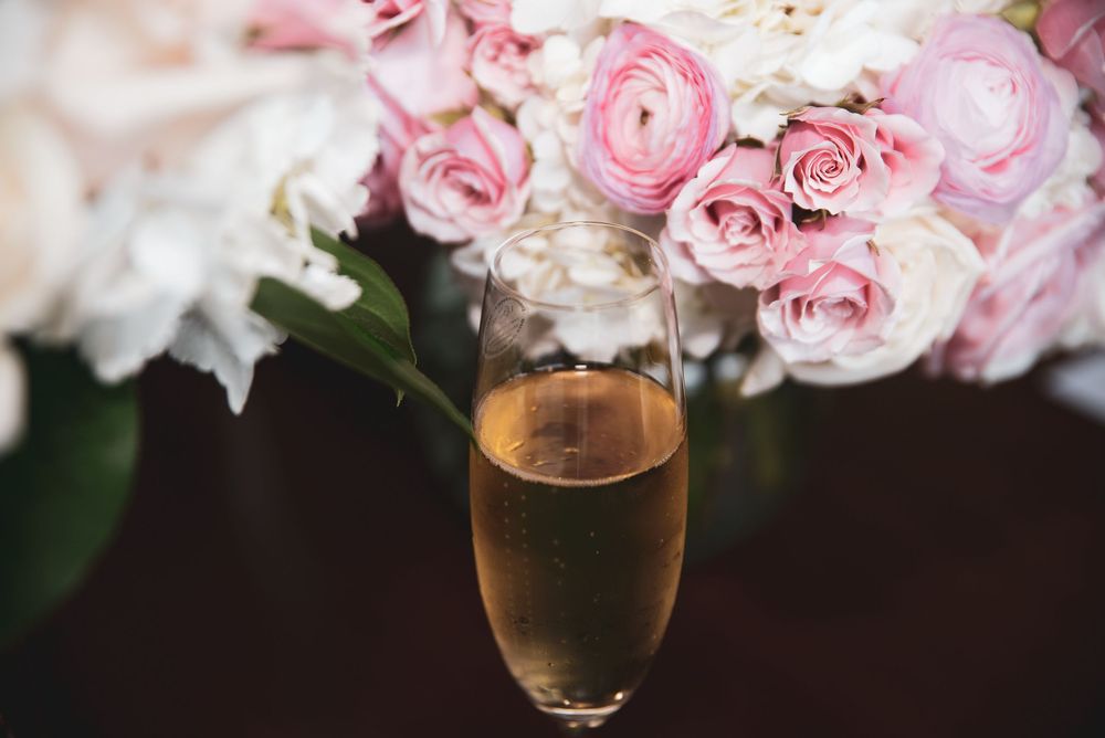 A champagne flute filled with sparkling wine sits in front of a lush bouquet of pink and white roses.