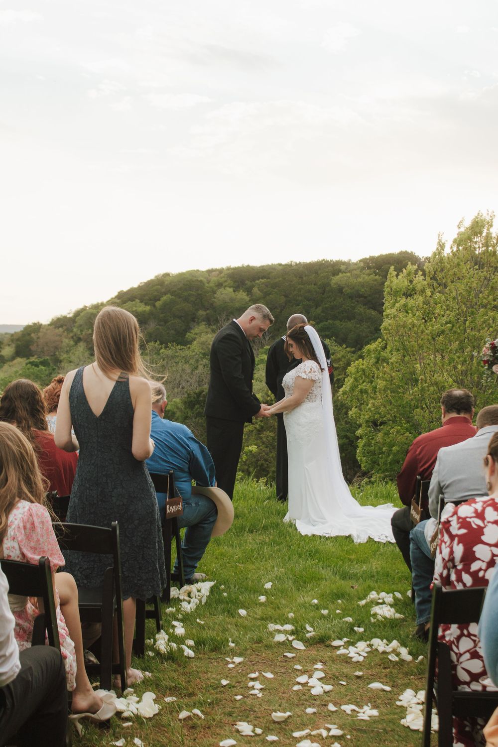 Outdoor wedding ceremony on a hillside with bride and groom holding hands before guests.