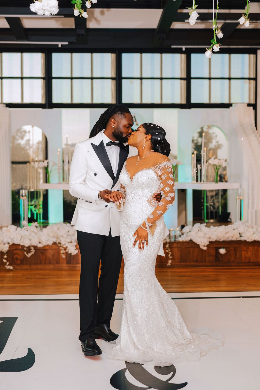 Newlyweds share a kiss on the dance floor, bride in lace gown and groom in white tuxedo jacket.