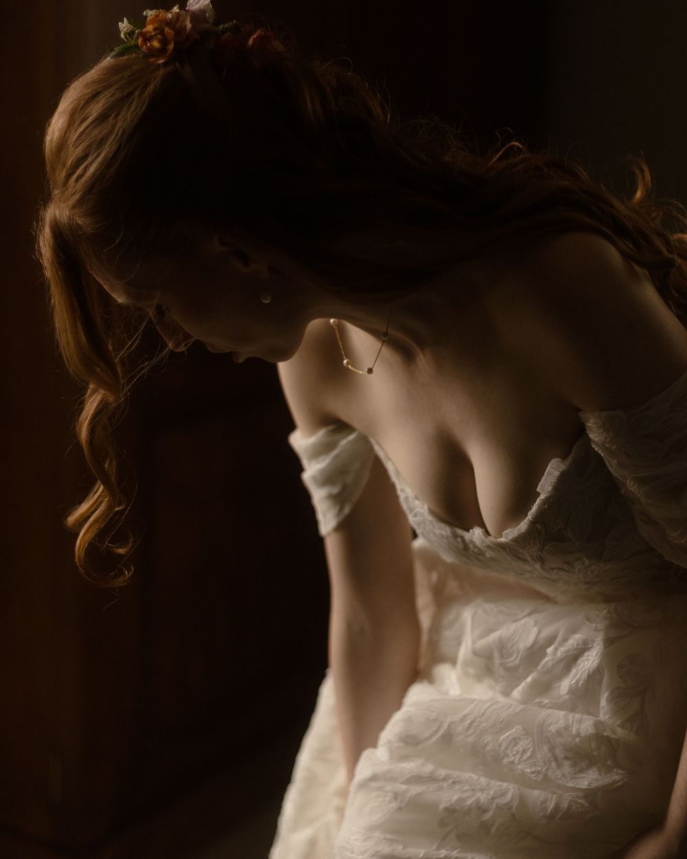 A bride in a white lace gown with floral hair accessory, captured in dramatic moody lighting.