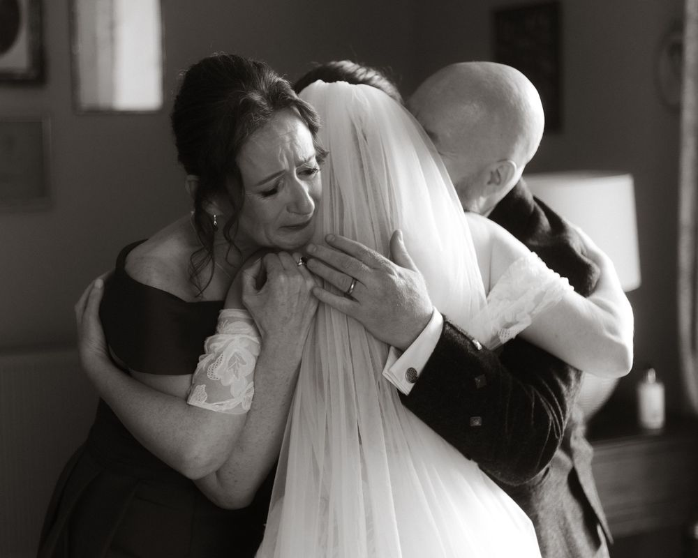 Emotional black and white wedding photo of bride sharing a heartfelt group hug with loved ones on her special day.
