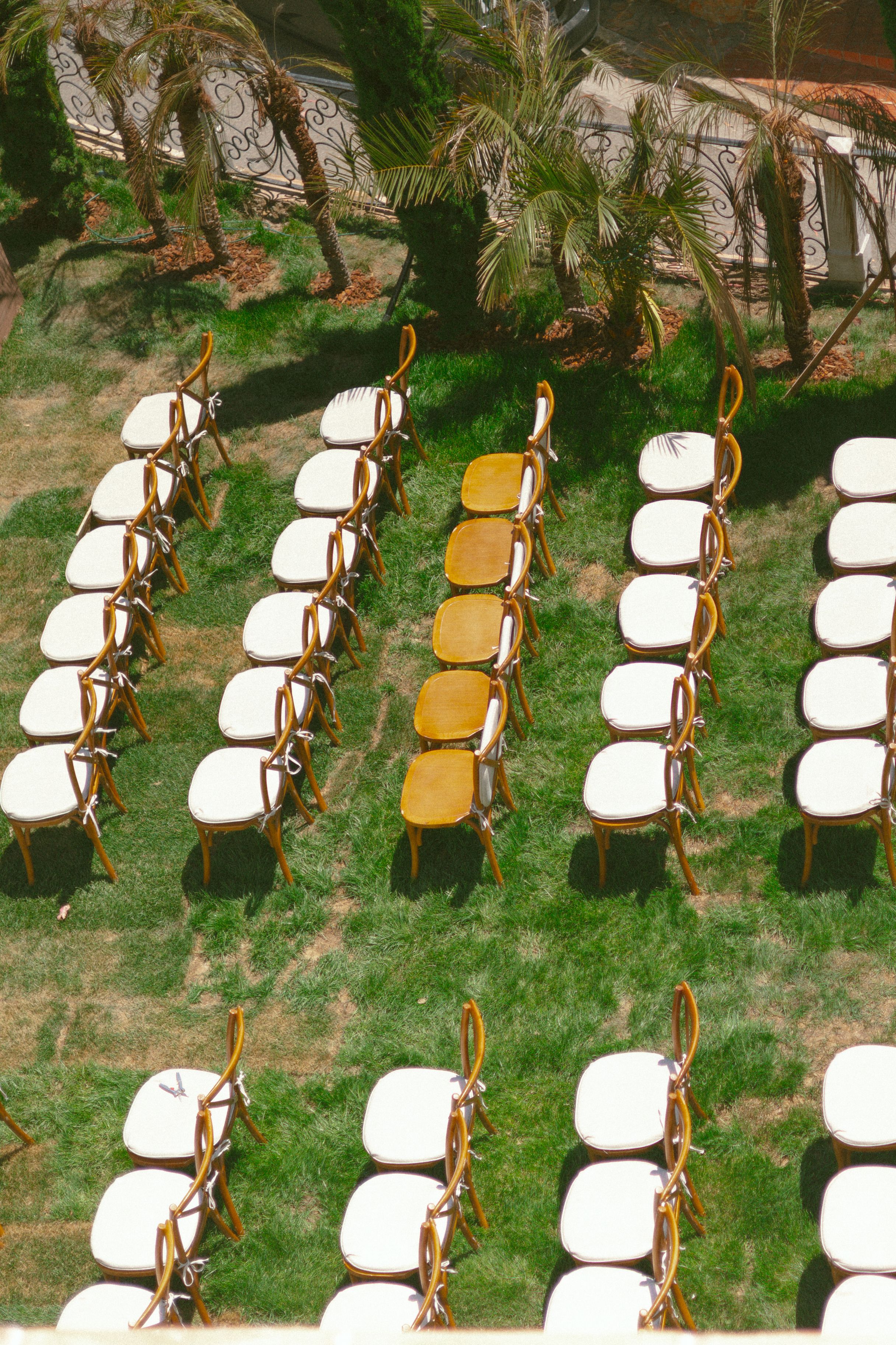 Aerial view of white cushioned chairs arranged in rows on green grass for an outdoor ceremony, with yellow chairs in the center.
