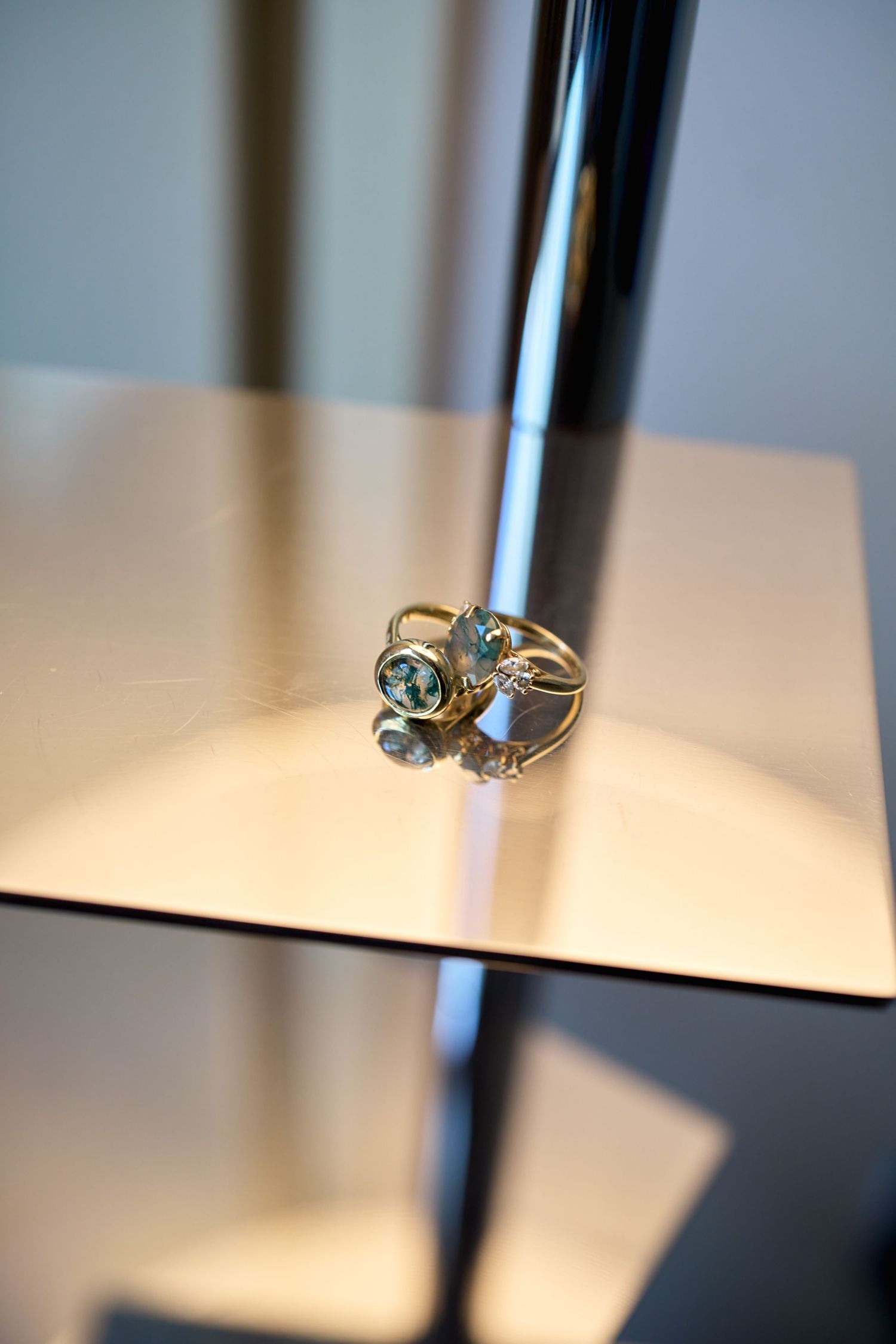 Gold ring with blue topaz gemstones displayed on a reflective surface near a chrome stand.