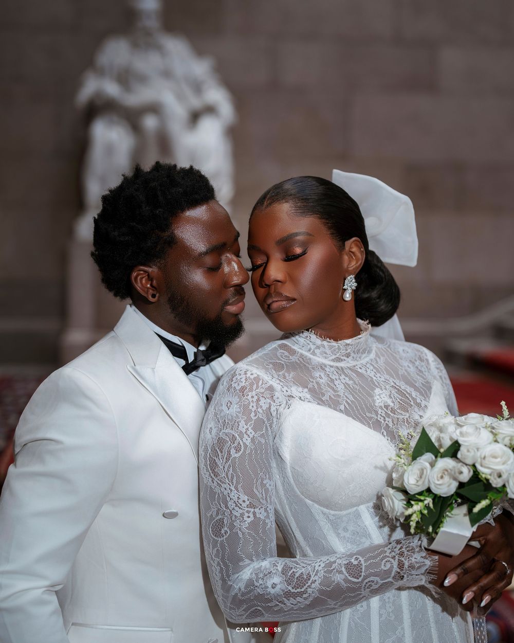 Elegant bride and groom in white wedding attire share an intimate moment inside a church.