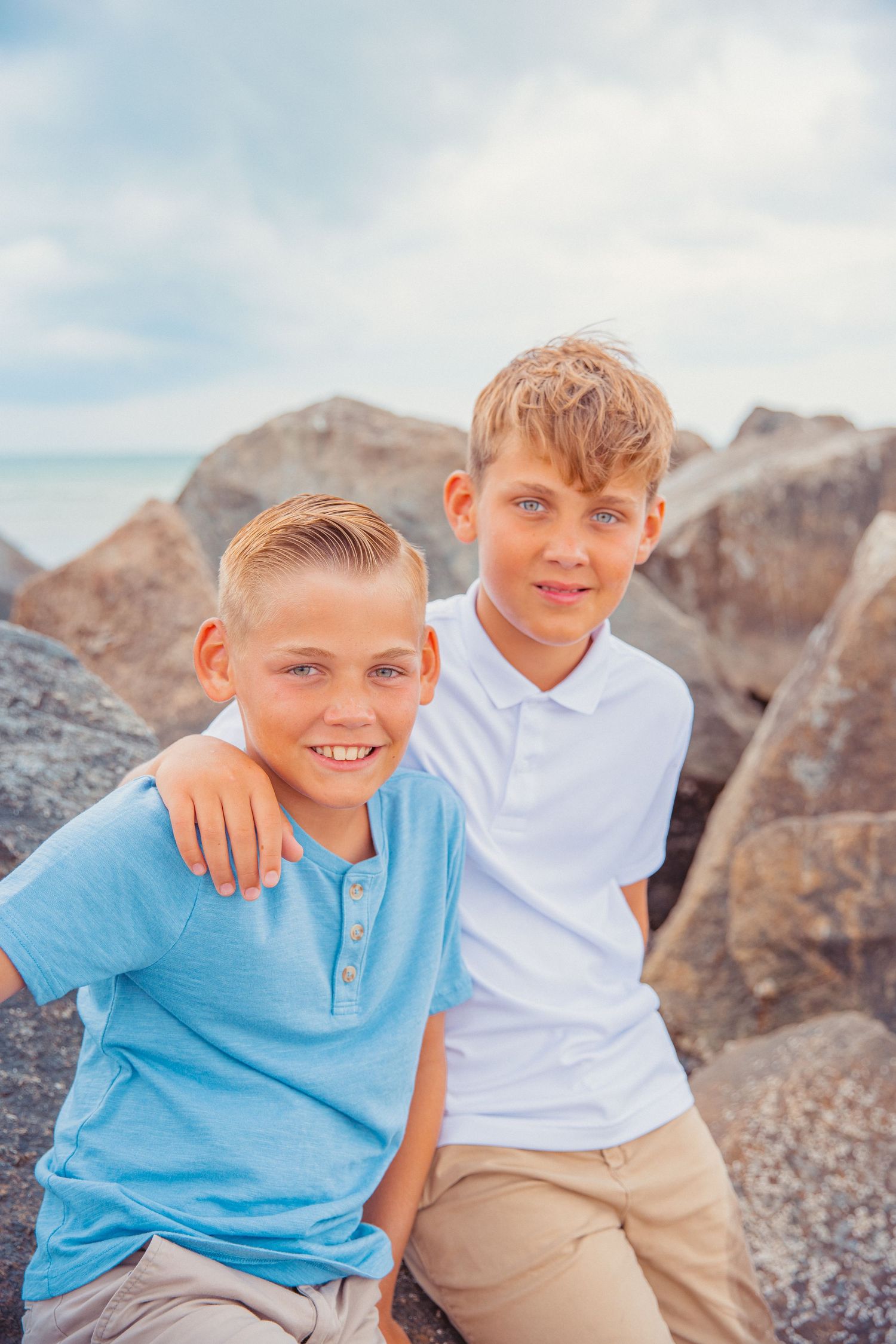 Two brothers smile for a picture while sitting on rocks at a beach jetty