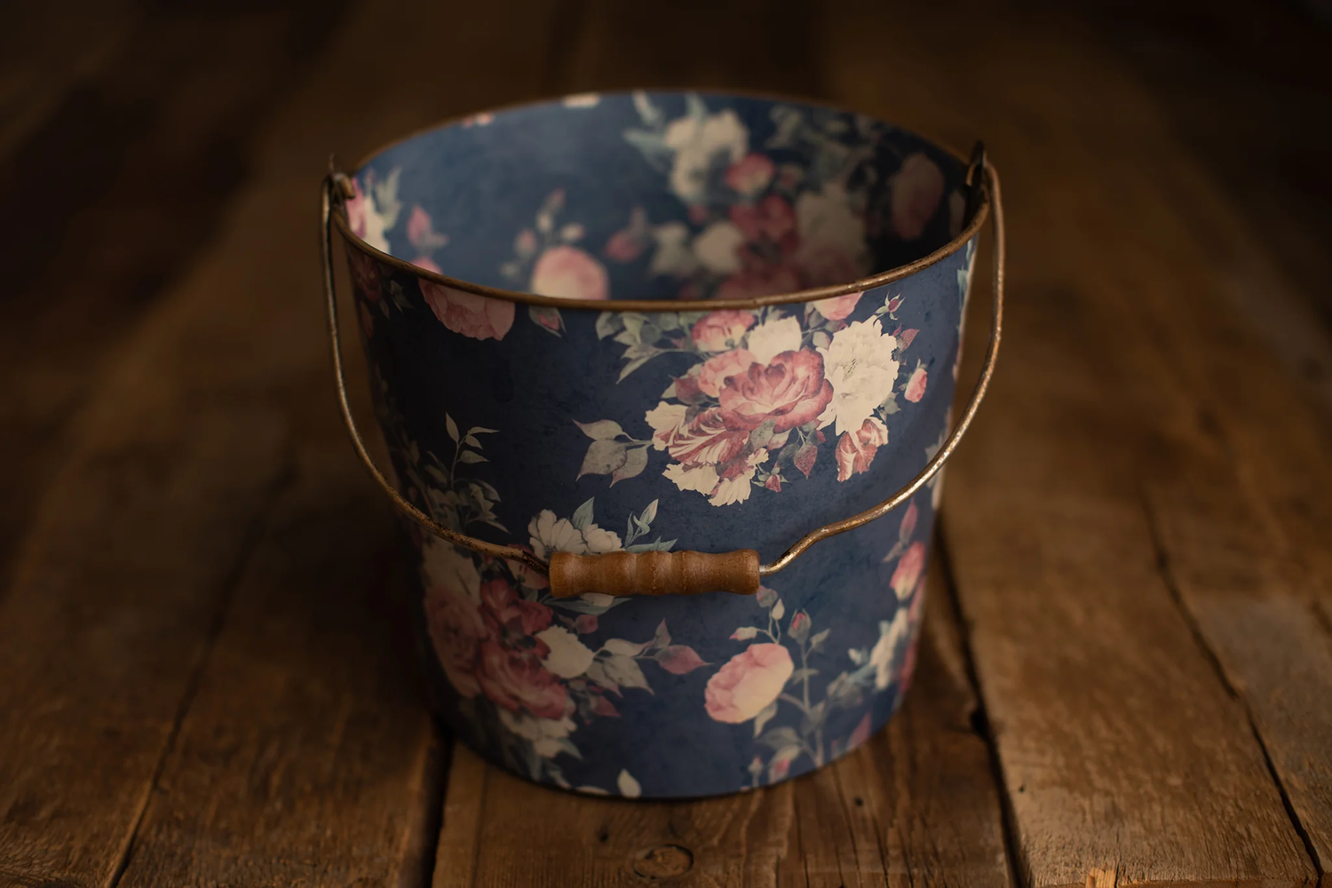 Navy blue floral metal bucket with gold handle on rustic wood floor.