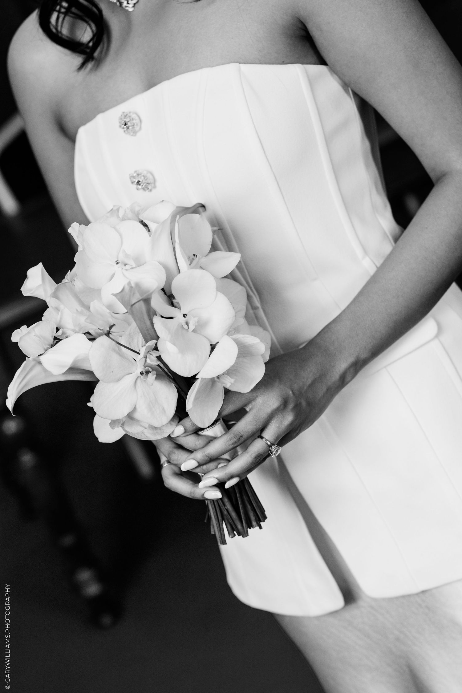 Bride in strapless white dress holding elegant orchid and calla lily bouquet, black and white wedding photo.