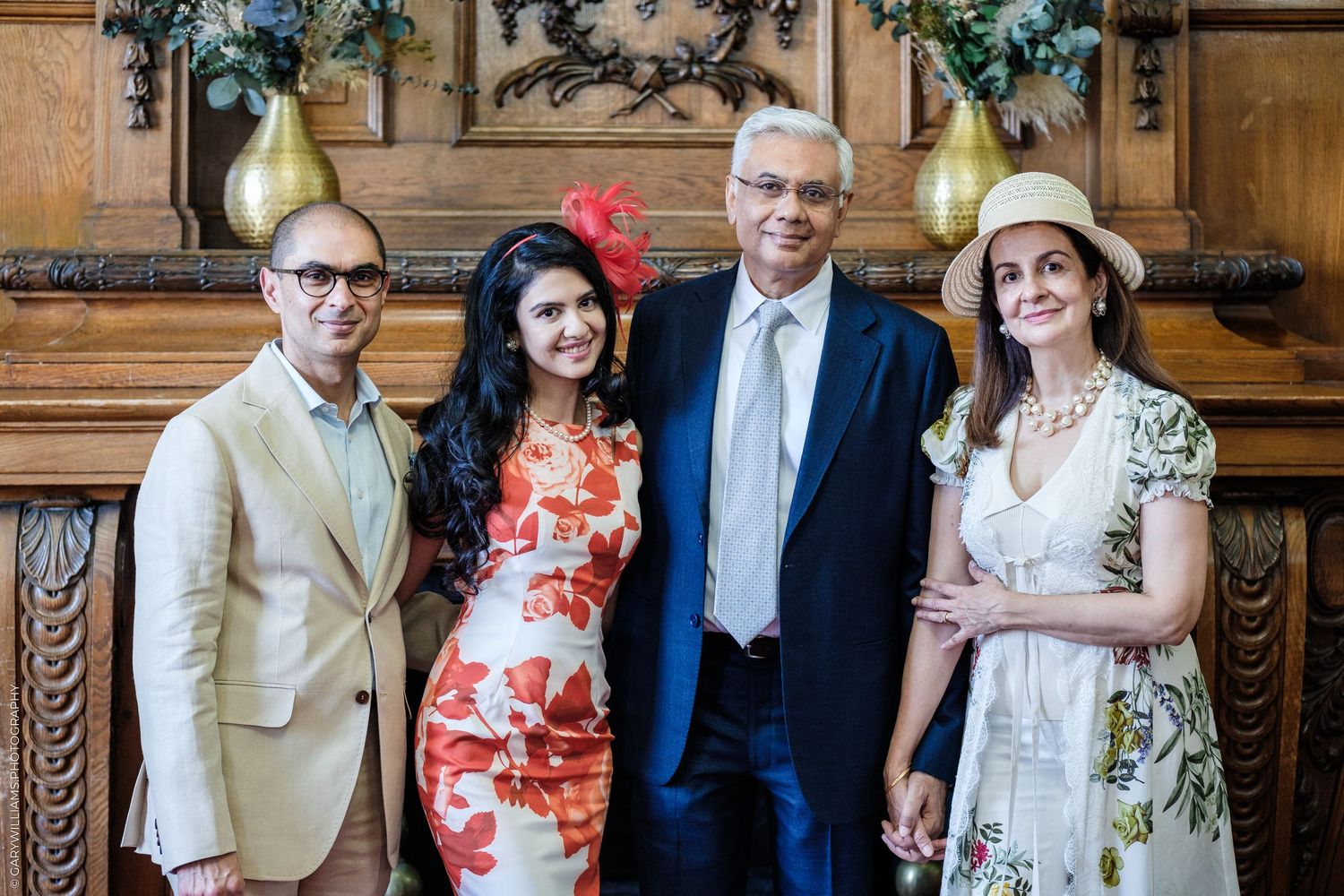 Four elegantly dressed people posing together at a formal event in a wood-paneled room.