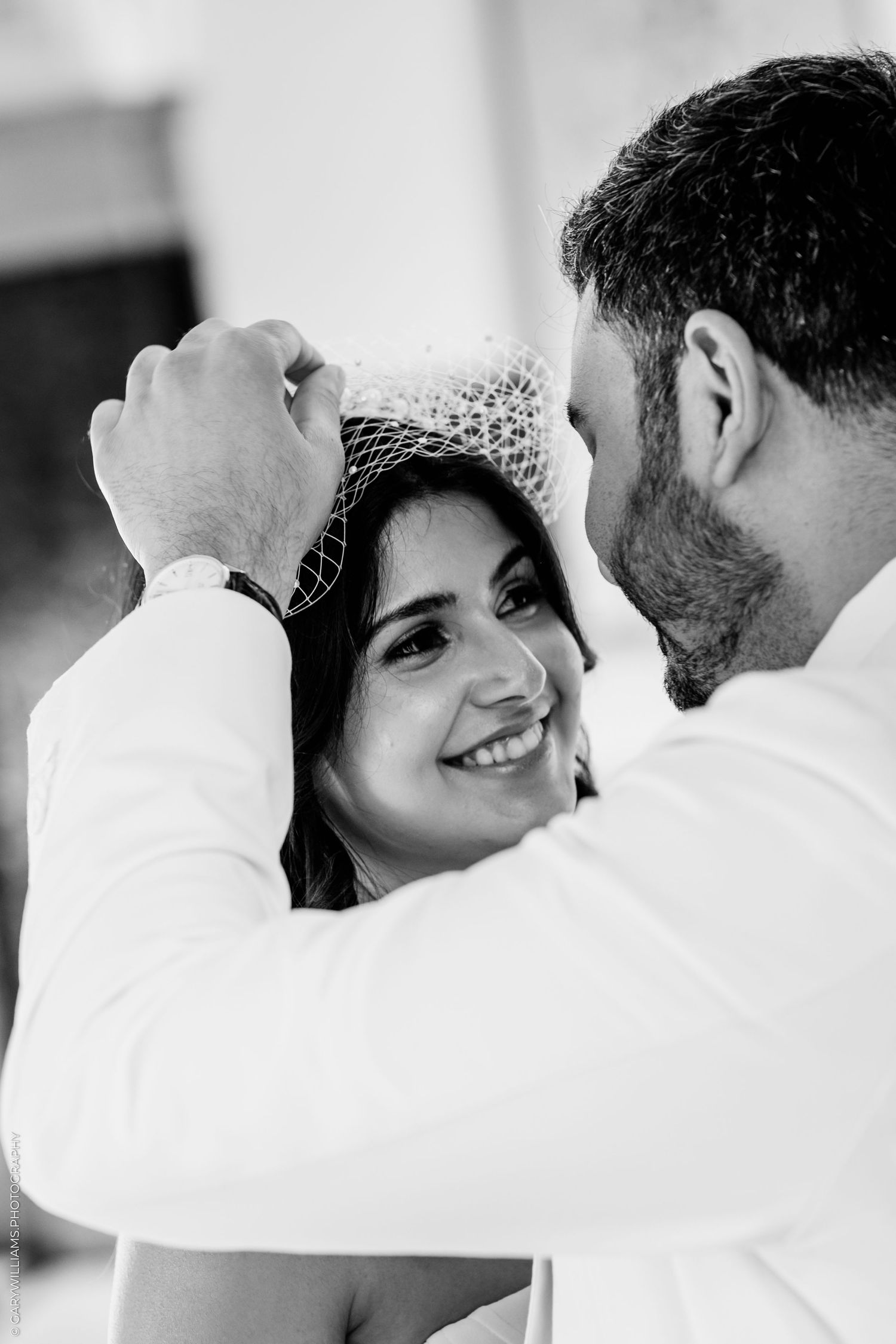 Groom placing a bridal veil on smiling bride in black and white wedding portrait.