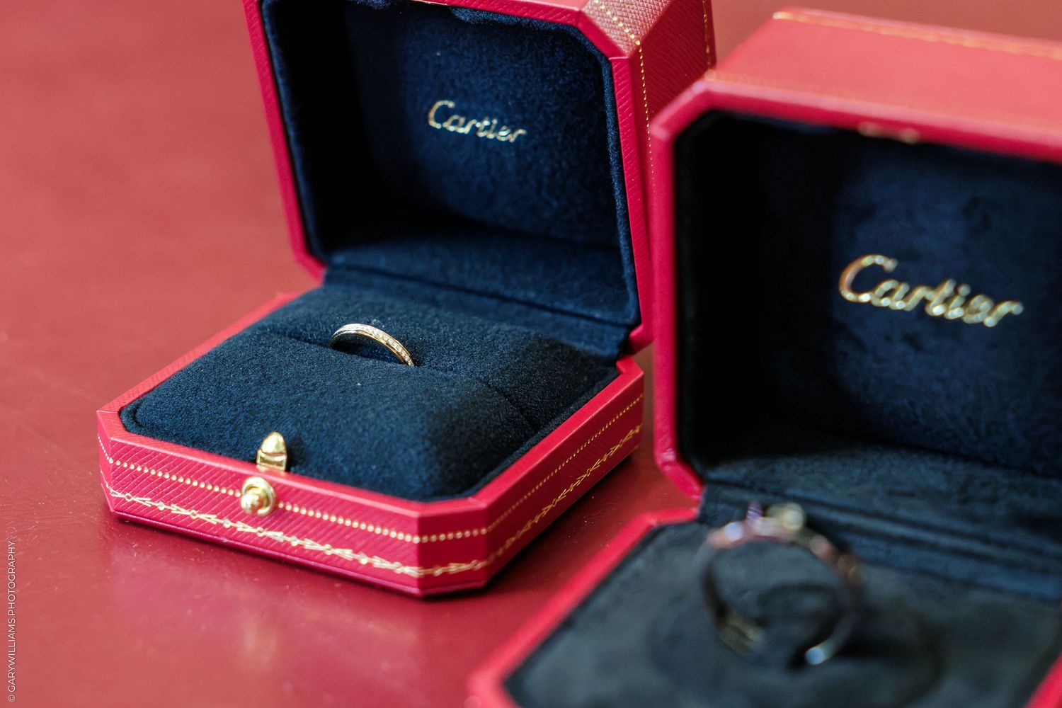 Two Cartier rings in open red luxury jewelry boxes displayed on a red surface.