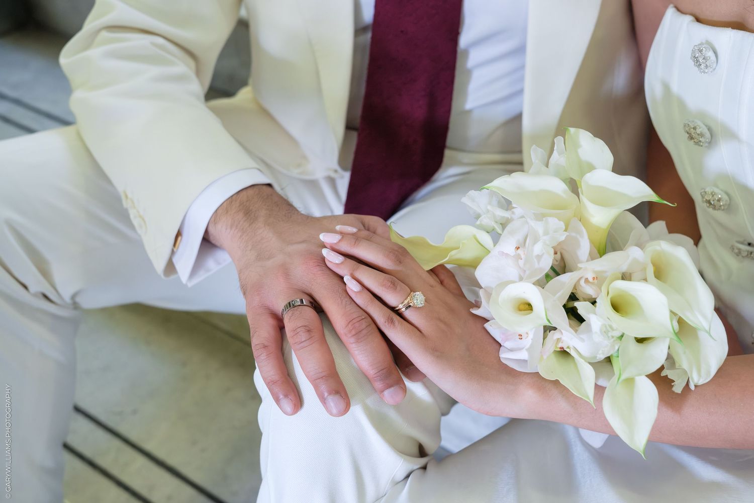 Bride and groom holding hands showing wedding rings with a white floral bouquet during wedding ceremony.