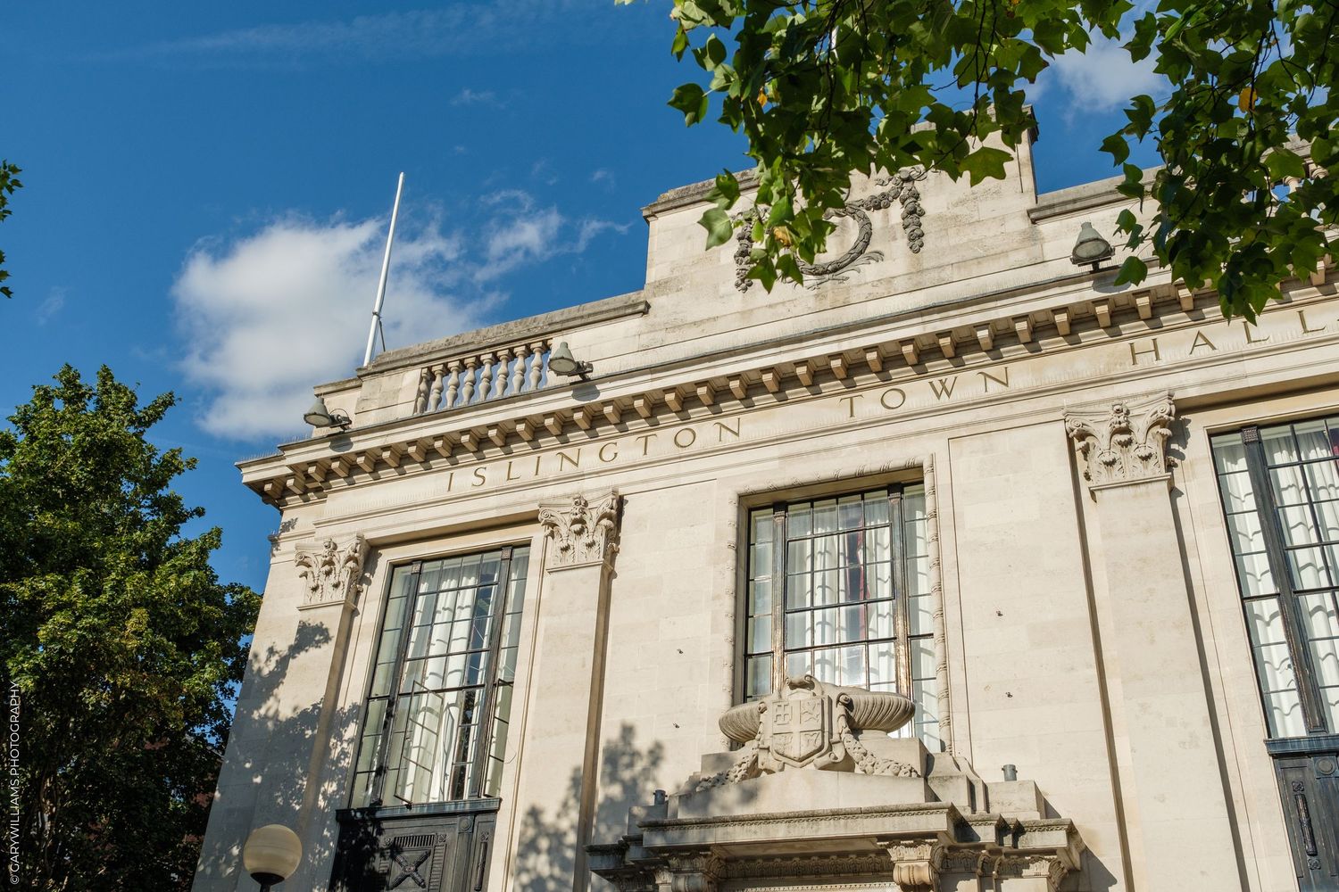 Exterior view of Wallingford Town Hall, a grand neoclassical stone building under a blue sky with trees.