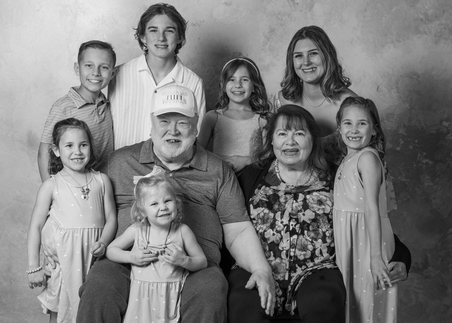 Happy family of four sitting together on white background, parents and two daughters smiling in casual clothes.