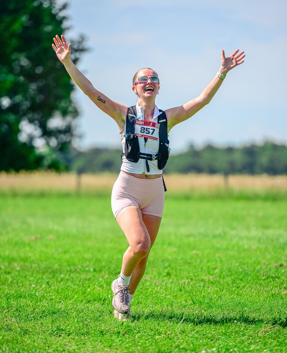 Jubilant female runner celebrates crossing the finish line at an outdoor summer race event.